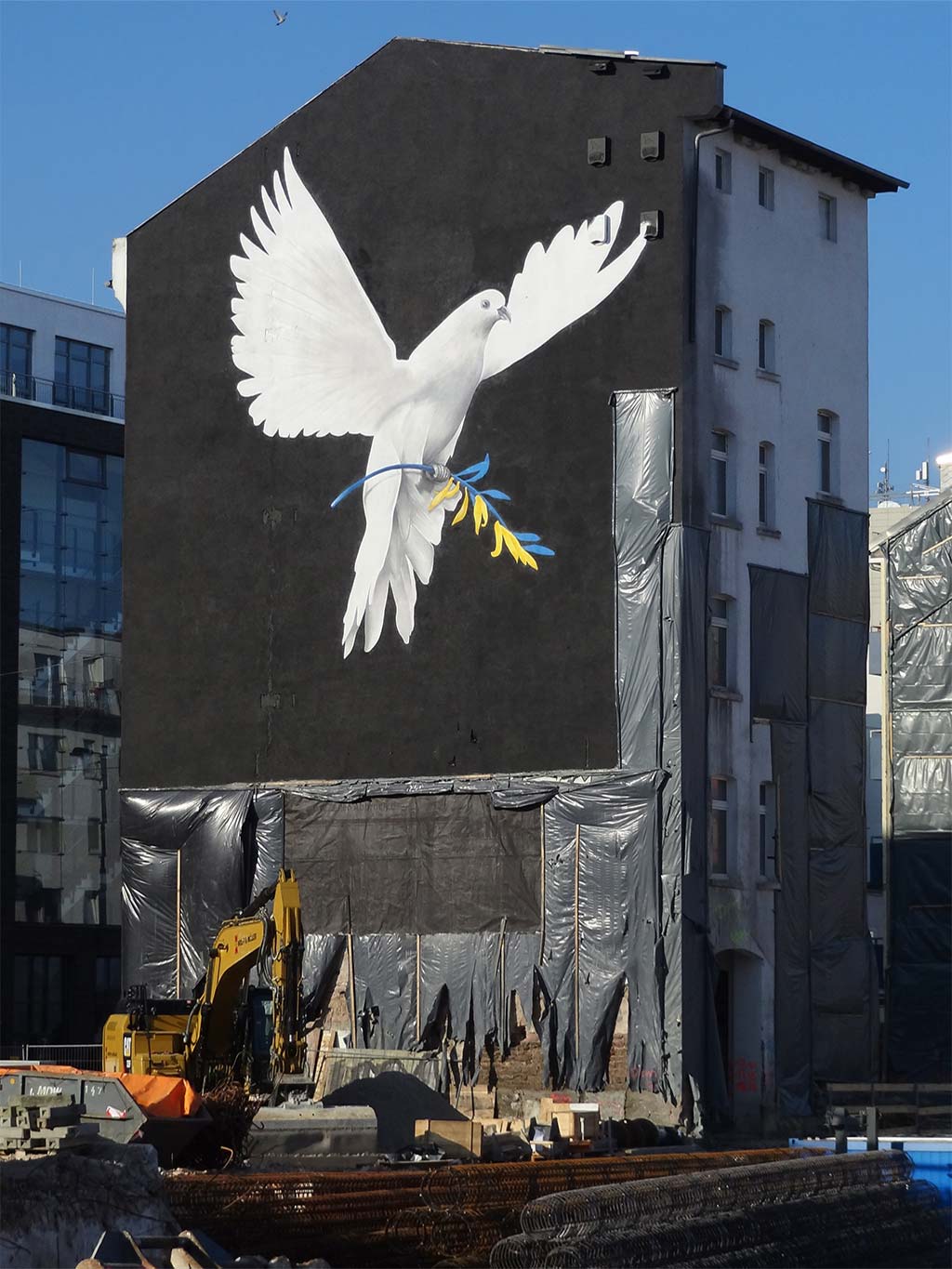 Wegen Krieg in der Ukraine: Hausfassade zeigt Friedenstaube mit Olivenbaumzweig in den Farben gelb und blau