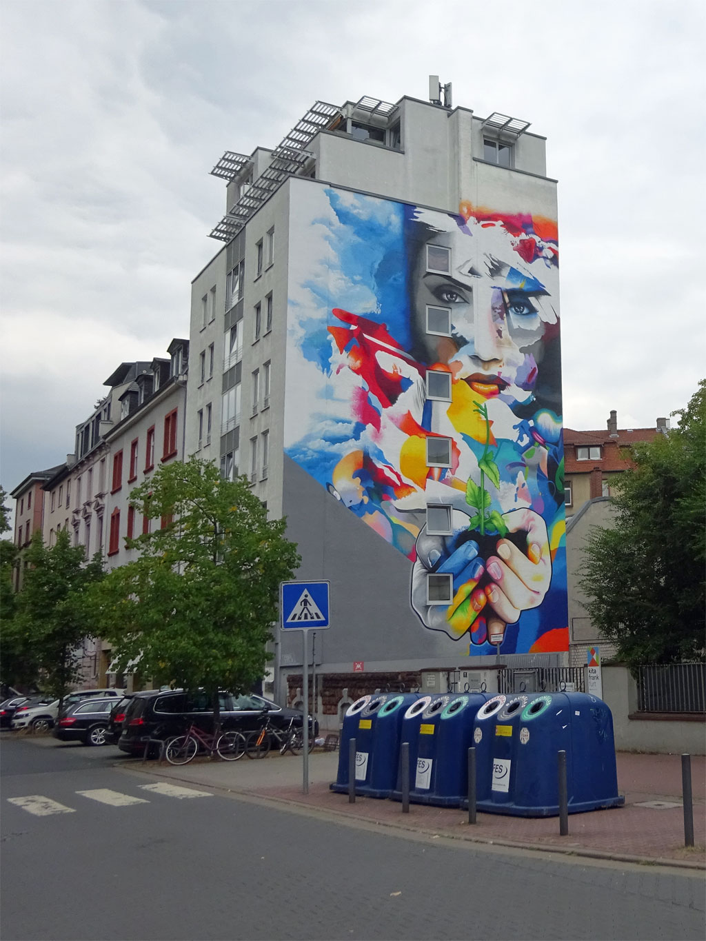 Großes Bild an HAusfassade zeigt eine Frau mit Erde und keimender Pflanze in den Händen